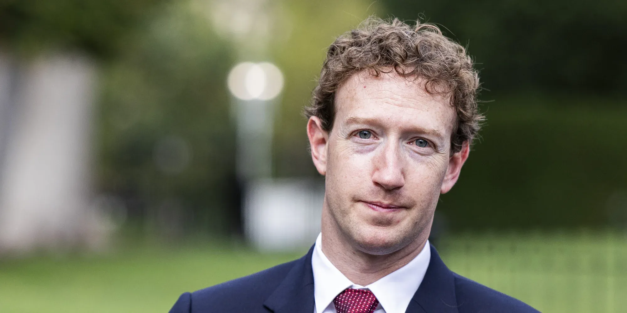 Mark Zuckerberg in a navy suit and red tie outdoors