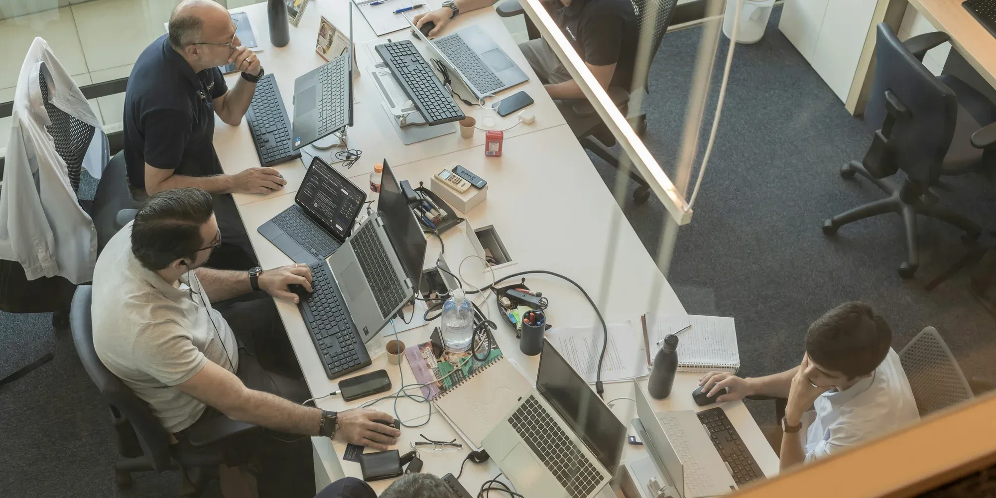 A team working at laptops on a shared office desk, seen from above